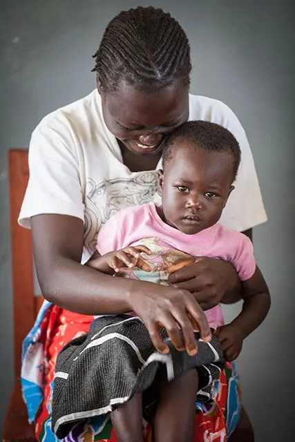 A mother laughs while holding her daughter on her lap.