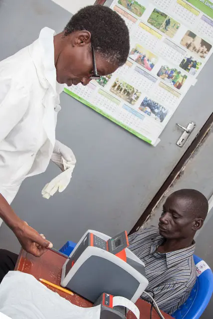 A health worker inserts a blood test in a PIMA machine, while a patient looks on.