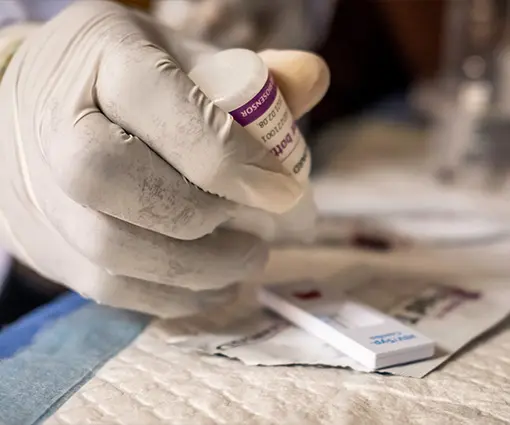 Close-up photo of a gloved hand using a dropper over a blood test