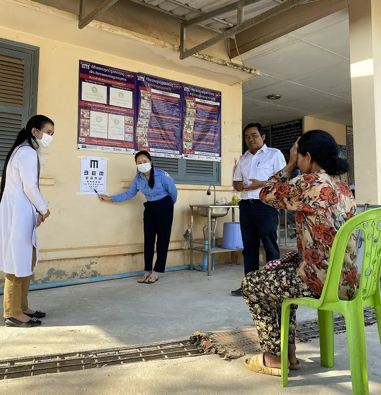 A Cambodian elderly lady covers one eye with her hand as her eye sight is tested