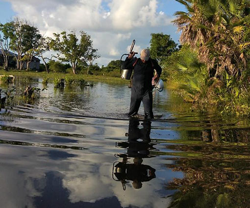 A malaria worker walks through water.