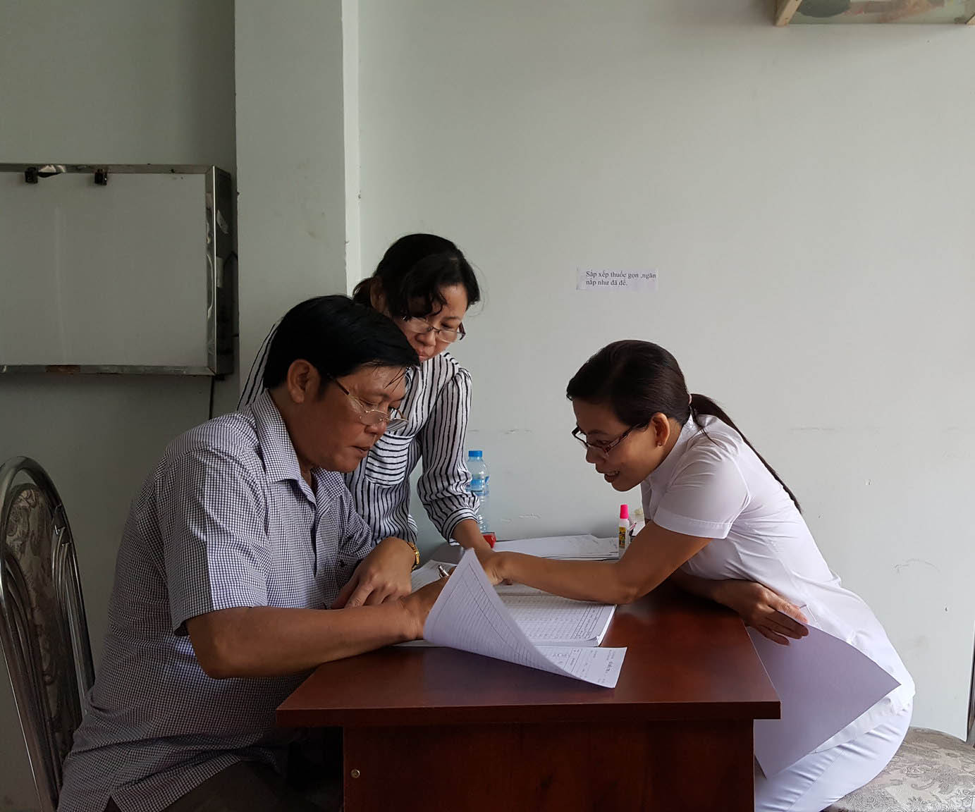 Three health workers in Vietnam huddle over a small table looking through paperwork.