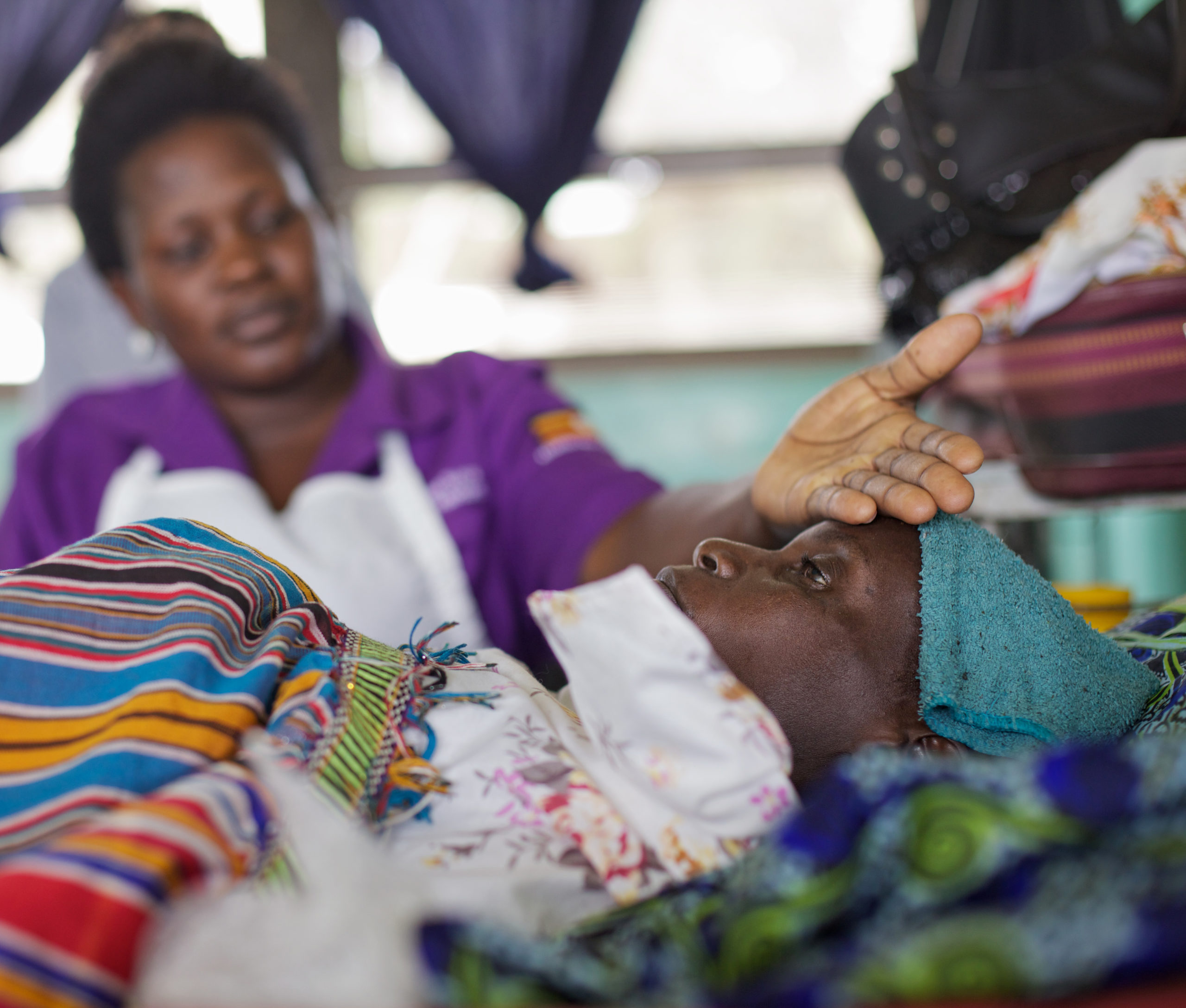 A nurse places her hand on the forehead of a cancer patient lying on a bed.