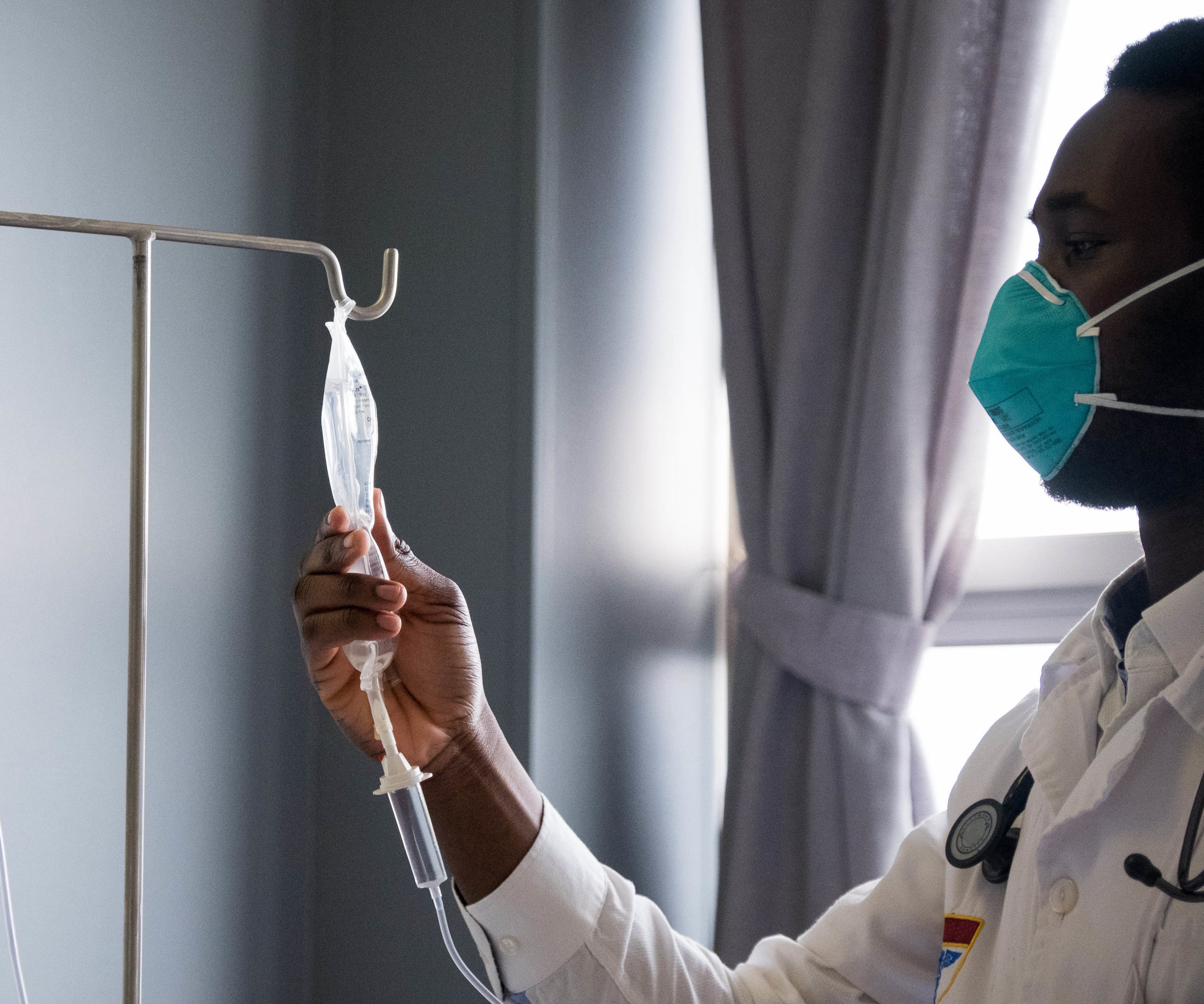 An African male healthcare worker checks the fluid levels in the patients IV drip