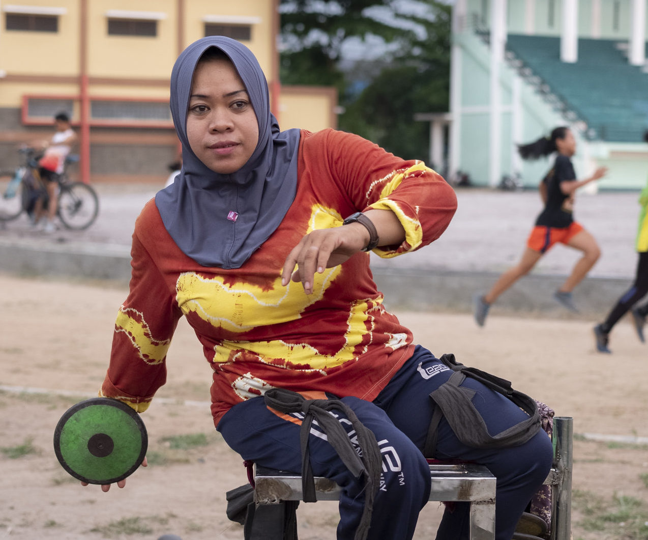 Half body shot of Rusmiyati from Indonesia throwing a discus while sitting on a throwing frame. Photo by Angus Stewart as part of the Global Disability Innovation Hub's AT2030 programme