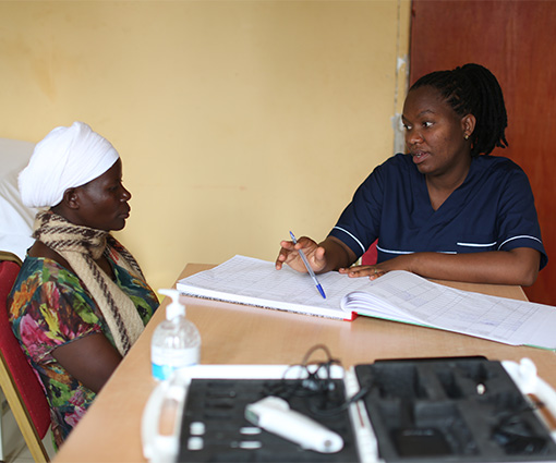 Female clinician speaks with a female patient at a table in Rwanda