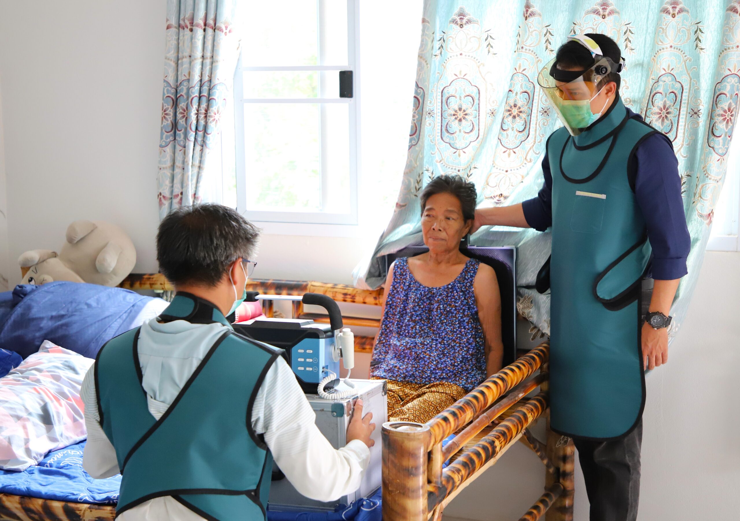 A woman sits before a digital chest x-ray for TB screening in Vietnam. One man sits before her operating the device, while the other stands behind her holding a plate on her back for the x-ray