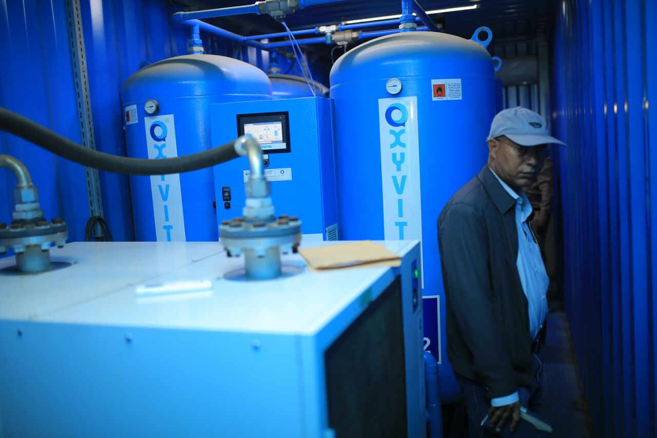 Man wearing a cap walks inside a shipping container containing an oxygen plant