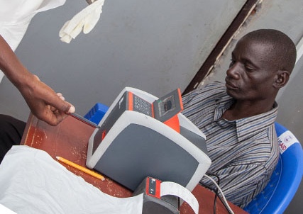 A health worker inserts a blood test in a PIMA machine, while a patient looks on.